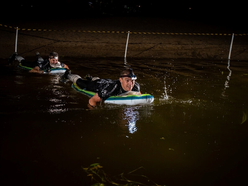 Võistlejad ujumas kummimadratsitel üle öise järve