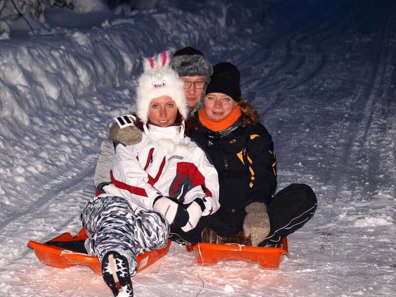 Kolm inimest kahe kelguga õhtuhämaruses lumisel talveteel